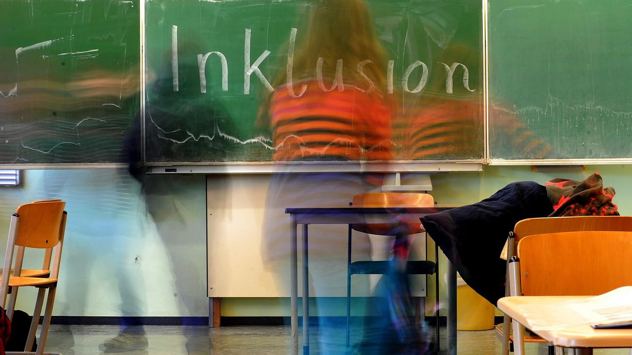 Ein Schulkind steht vor einer Tafel, auf der das Wort "Inklusion" geschrieben steht.