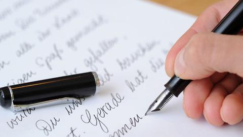 Die Hand einer Frau, die einen Brief mit einem Füllfederhalter schreibt.