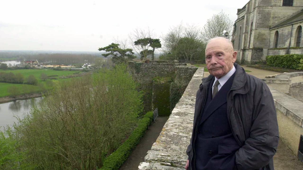 Der 2007 verstorbene Autor Schriftsteller Julien Gracq auf einer Aufnahme von 2003. Er steht in dunkler Kleidung an einer Steinmauer, die an das Ufer eines daruntergelegen Flusses grenzt.