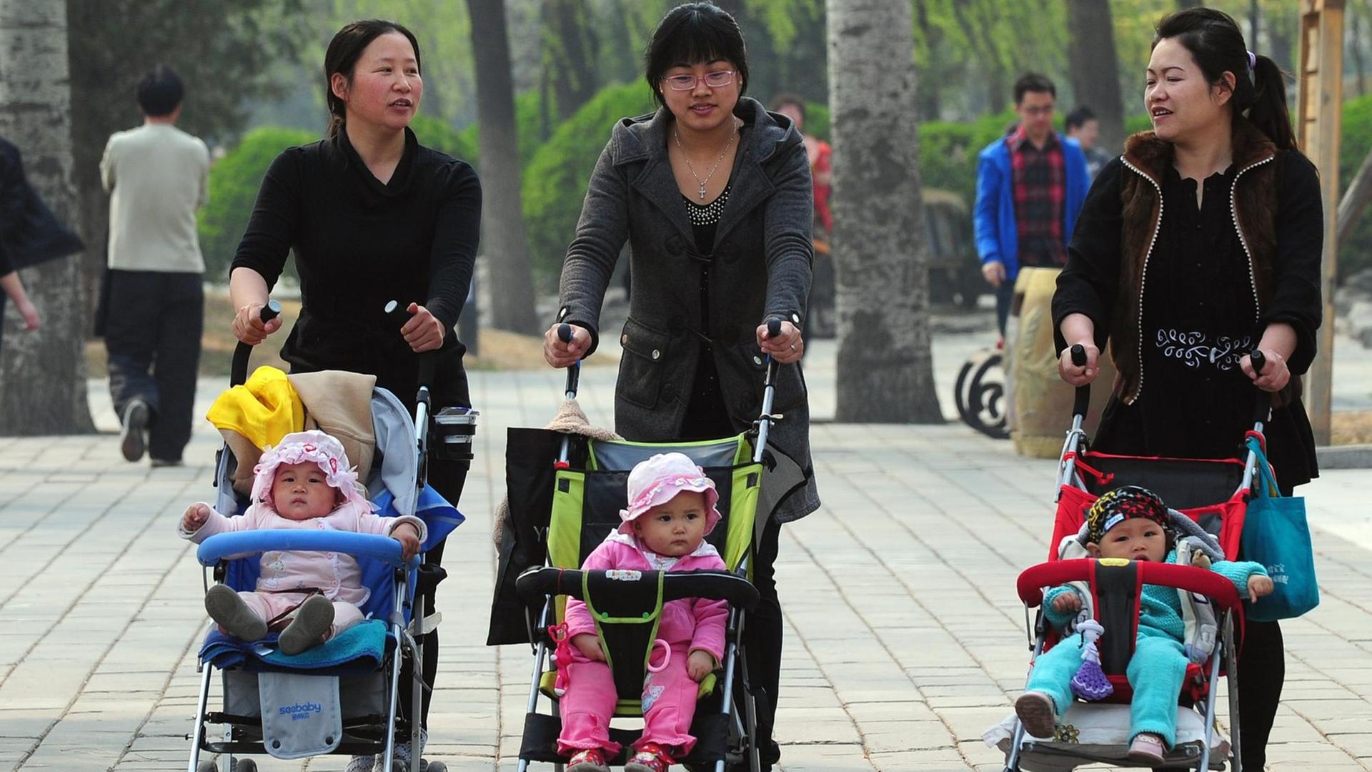 Frauen gehen mit Kinderwagen durch einen Park in Peking.