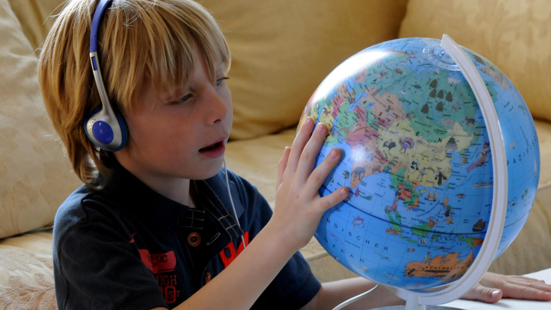 Ein sechsjähriges Kind sitzt mit Kopfhöhrern vor einem Globus.