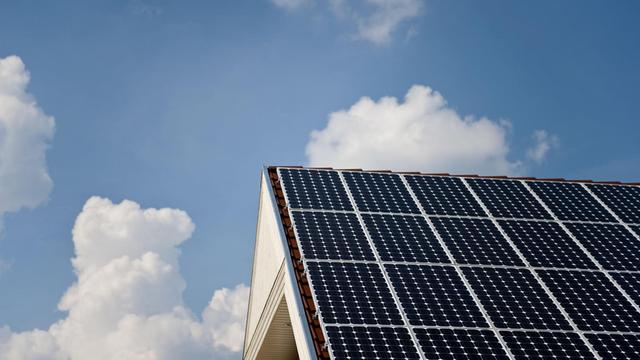 Ein Solardach auf einem Wohnhaus ist vor weiß-blauem Himmel zu sehen.