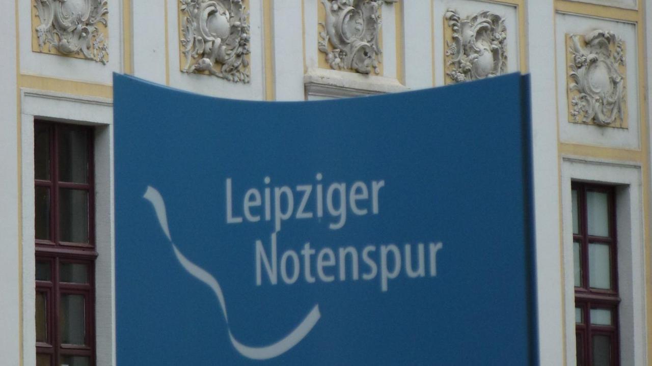 Das weiße Band und der Schriftzug der Notenspur auf einer blauen Infosäule in Leipzig.