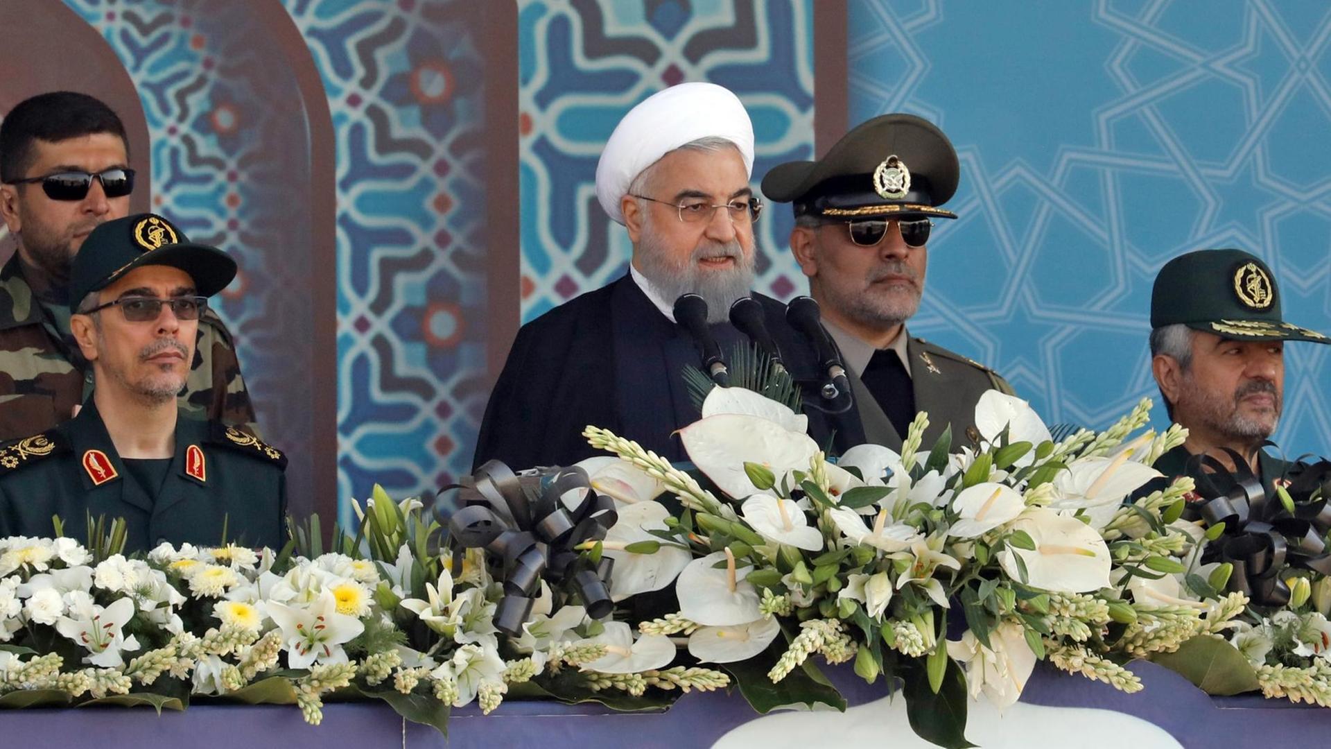 Irans Präsident Hassan Rohani bei einer Rede während einer Militärparade in Teheran. Hinter ihm stehen Angehörige der Armee.