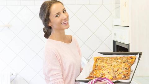 Eine Frau backt in ihrer Küche Pizza.