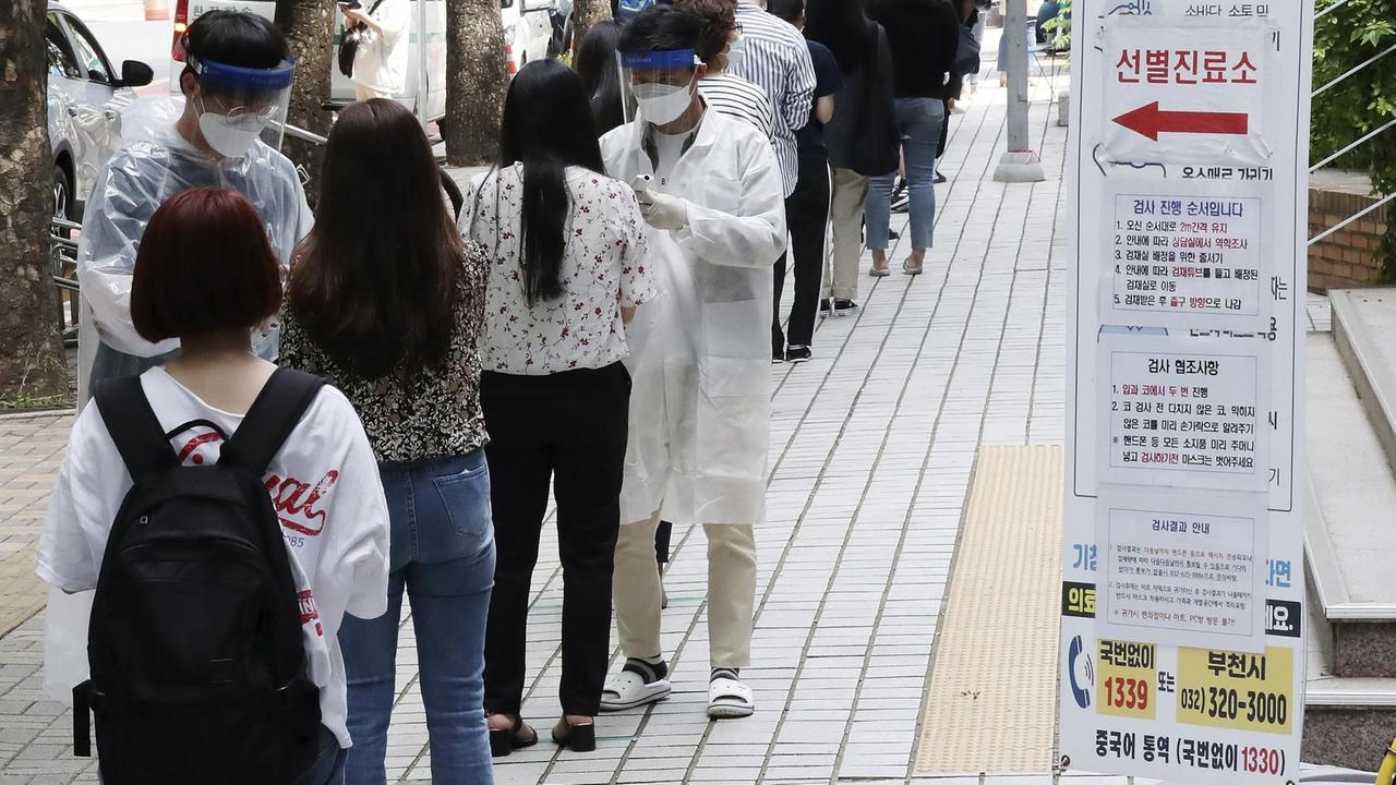 Südkorea, Bucheon: Menschen, bei denen der Verdacht besteht, dass sie mit Covid-19 infiziert sind, warten in einer Coronavirus-Screening-Station in einer Schlange darauf, vom dortigen Gesundheitspersonal in Schutzanzügen und Gesichtsvisieren getestet zu werden.
