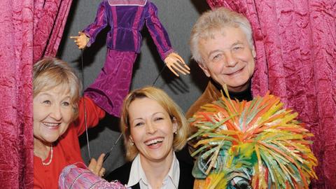 Die Schauspieler des «Velvets Theater» in Wiesbaden (v.l.n.r.) Dana Bufková, Barbara Naughton und Bedrich Hányš halten Stockpuppen und Masken vor einem roten Samtvorhang