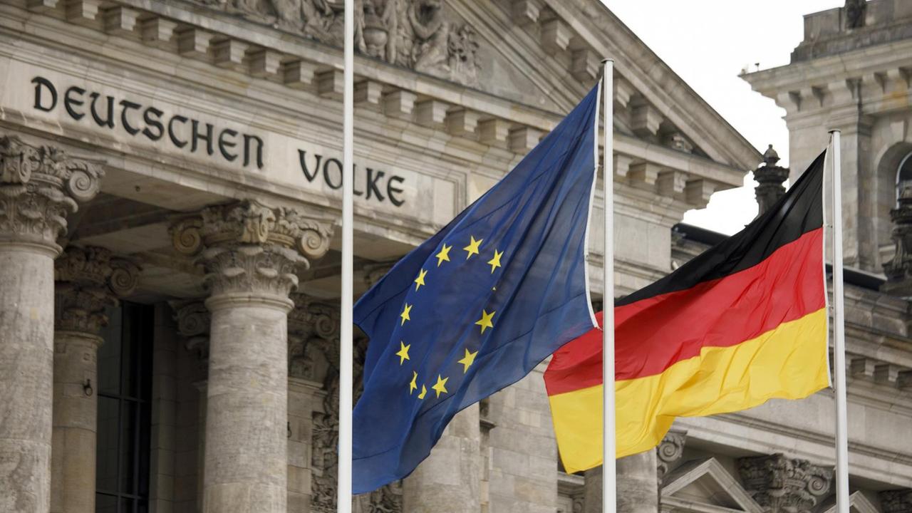 Eine Deutschlandflagge und eine Europaflagge wehen vor dem Reichstagsgebäude, dem Sitz des Deutschen Bundestages.