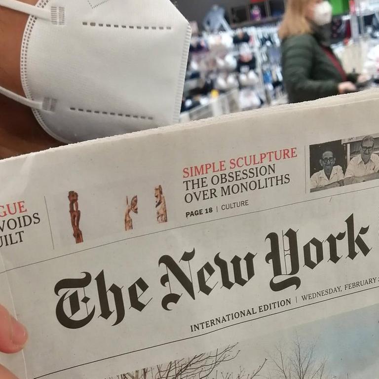 Eine Frau mit FFP2-Maske hält eine Printausgabe der "New York Times" in der Hand