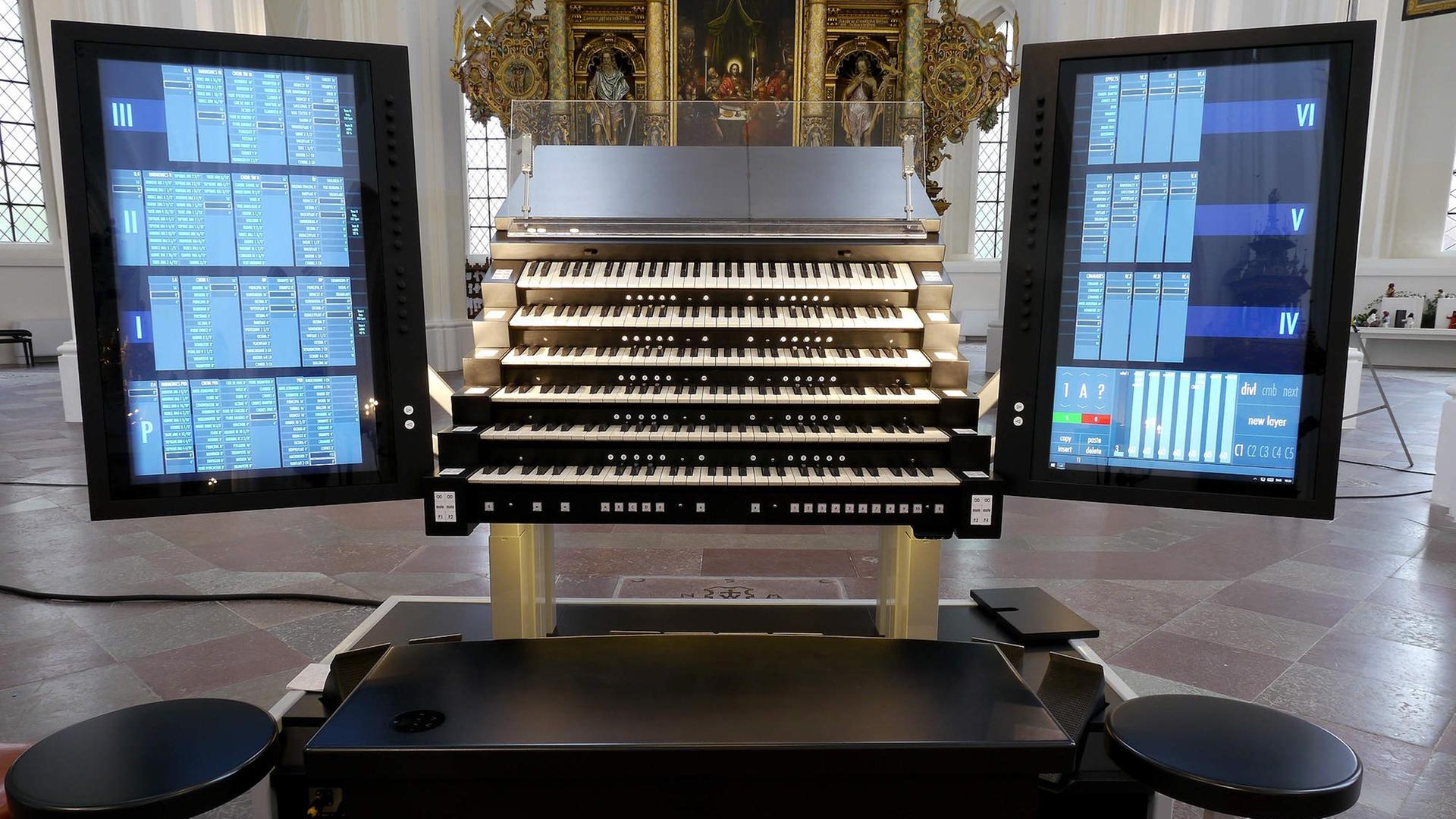 Der moderne Spieltisch der Orgel in der St.Petri-Kirche in Malmö, mit 6 Manualen und zwei großen Computer-Touch-Bildschirmen an der linken und rechten Seite. Im Hintergrund der barocke Altar