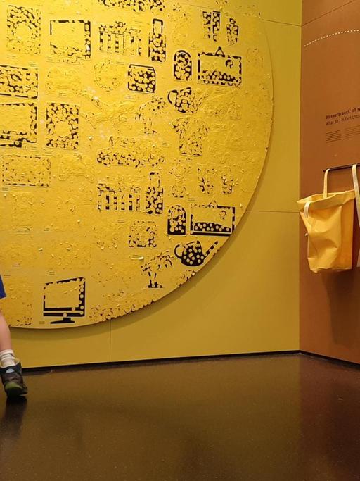 Ein Junge steht vor einer gelben Wand und klebt Punkte auf die Bilder eines Autos oder ein Flugzeugs.