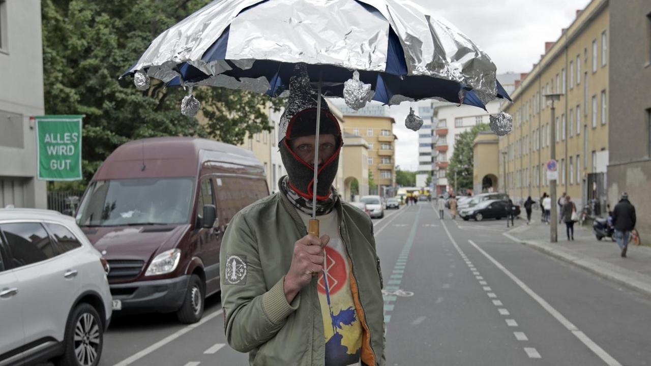 Ein Demonstrant mit Maske und Aluminiumschirm steht auf der Straße in Berlin.