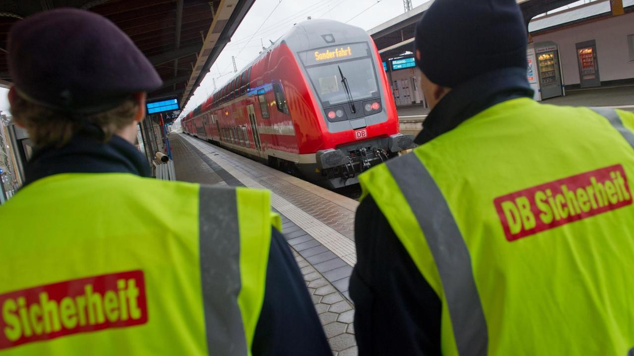 Im Vordergrund sieht man zwei Mitarbeiter des Sicherheitspersonals der Deutschen Bahn. Im Hintergrund eine Regionalbahn RE 5 im Bahnhof von Stralsund (Mecklenburg-Vorpommern). 