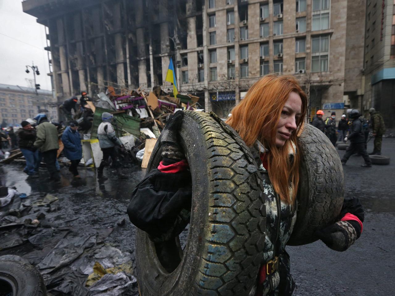 Eine Frau trägt Reifen zur Errichtung einer Barrikade auf den Maidan. Im Hintergrund Rauchwolken. Eine Frau trägt Reifen zur Errichtung einer Barrikade auf den Maidan. Im Hintergrund Rauchwolken.