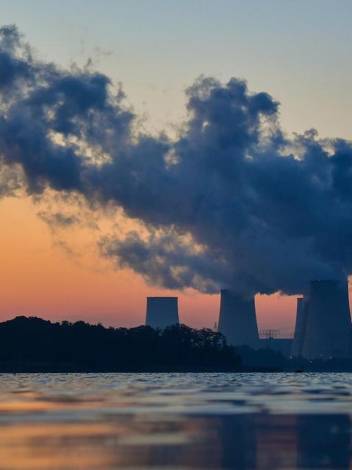 Wasserdampfschwaden steigen vor Sonnenaufgang in den farbigen Morgenhimmel aus den Kühltürmen des Braunkohlekraftwerkes Jänschwalde der LEAG (Lausitz Energie Bergbau AG) hinter einem Karpfenteich in Peitz (Brandenburg).