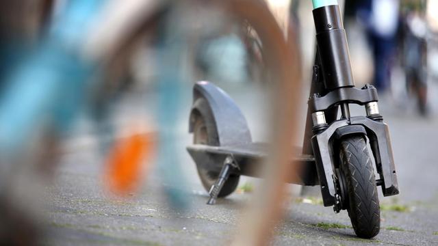 Ein E-Tretroller der Verleihfirma "Tier" steht in der Innenstadt hinter einem abgestellten Fahrrad.