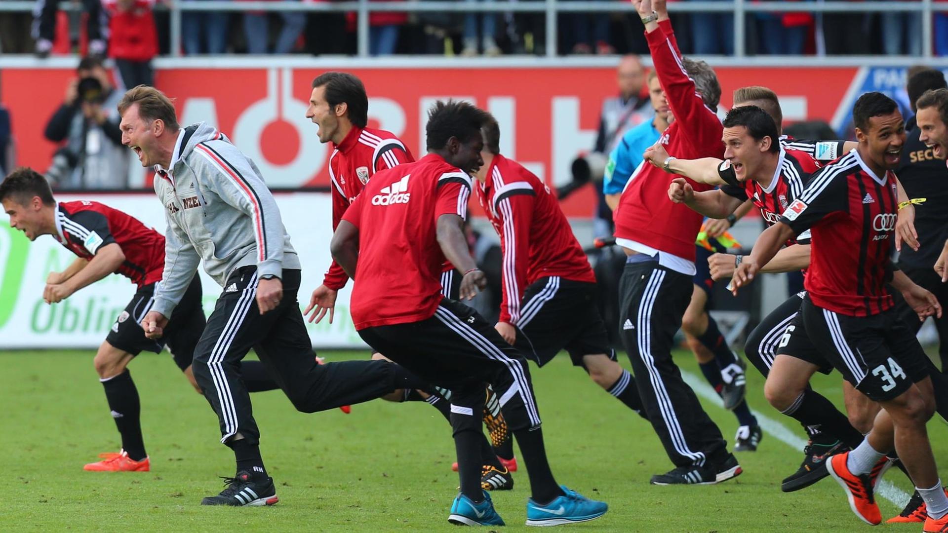 Die Spieler des FC Ingolstadt stürmen nach dem Abpfiff der Partie gegen RB Leipzig jubelnd über den Platz und feiern den vorzeitig gesicherten Bundesliga-Aufstieg. Die Spieler tragen schwarz-rote-Trikots. In erster Reihe jubelt auch Trainer Ralph Hasenhüttl