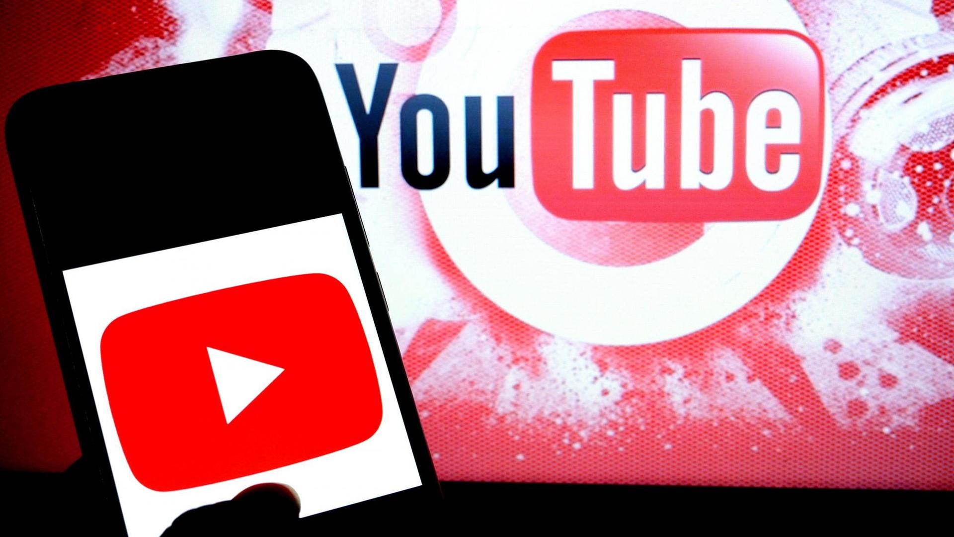 Handy mit Youtube-Logo vor einer Leinwand, die ebenfalls das Youtube-Logo zeigt