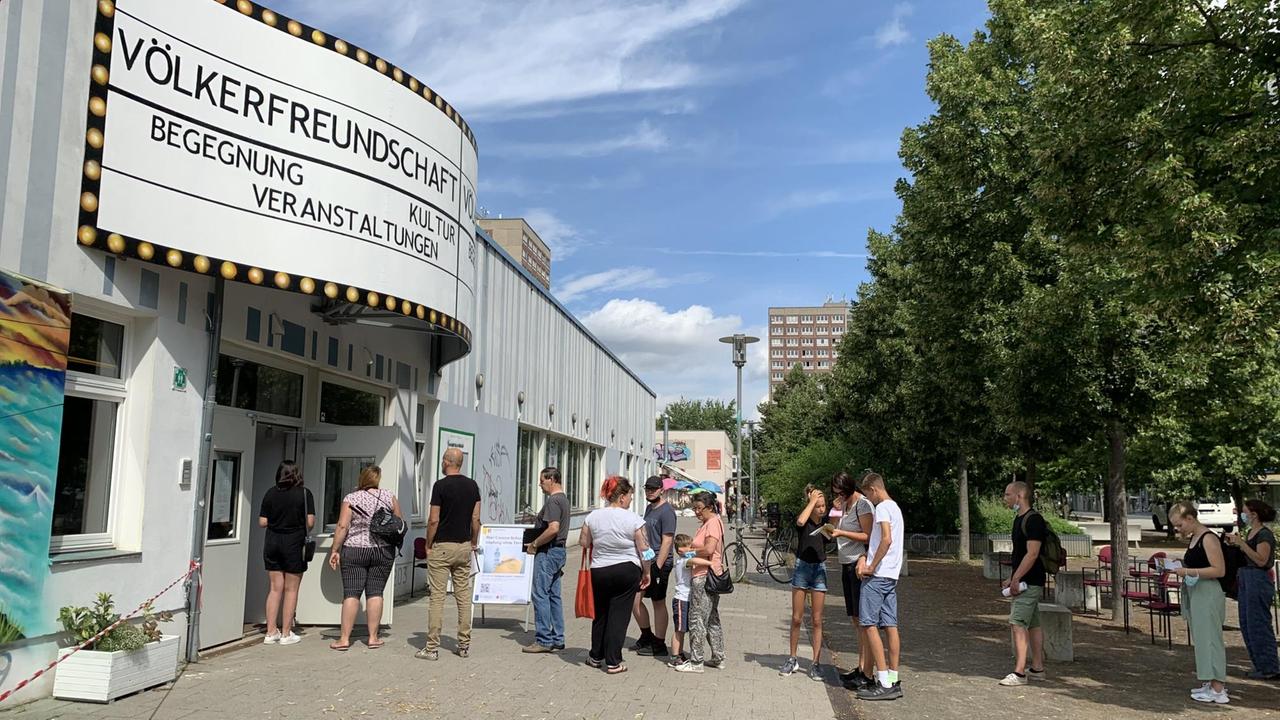 Menschen stehen in Leipzig vor einem Gebäude Schlange und warten auf ihre Coronaimpfung.