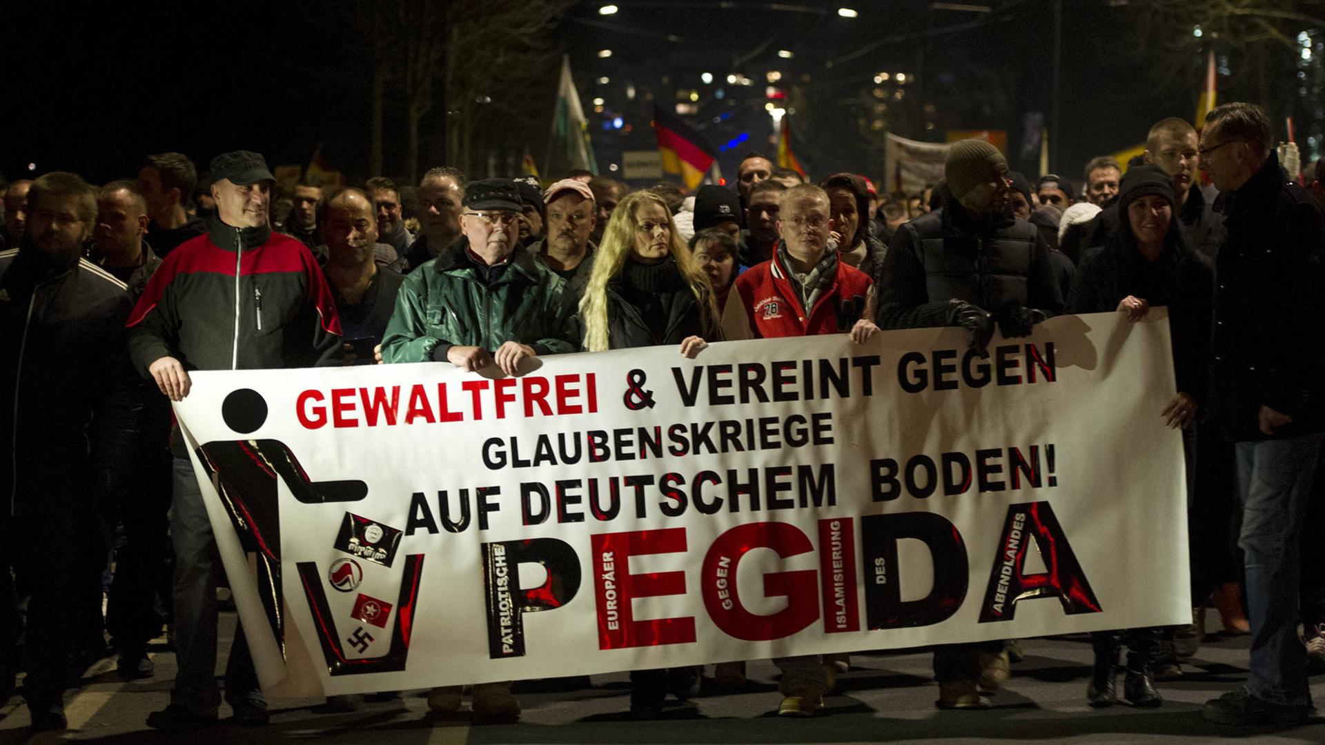 Mehrere Pegida-Demonstranten halten ein Banner mit der Aufschrift "Gewaltfrei und vereint gegen Glaubenskriege auf deutschem Boden!"