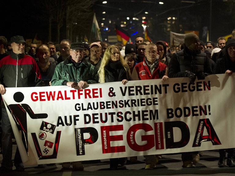 Mehrere Pegida-Demonstranten halten ein Banner mit der Aufschrift "Gewaltfrei und vereint gegen Glaubenskriege auf deutschem Boden!"