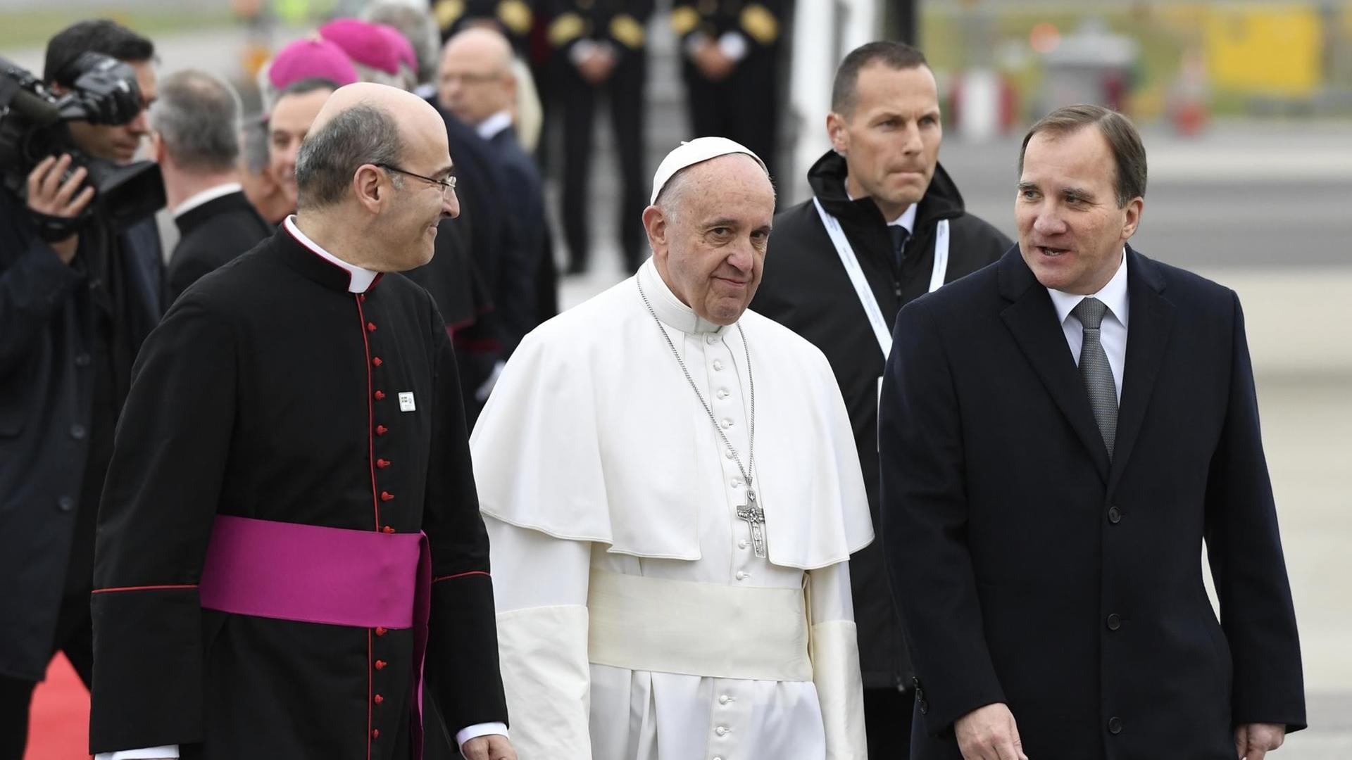 Papst Franziskus geht zwischen einem hohen katholischen Geistlichen (links) und Schwedens Premierminister Stefan Loefven.