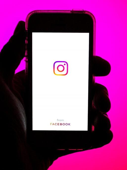 Eine Hand hält ein Smartphone mit dem Instagram Logo auf dem Bildschirm.