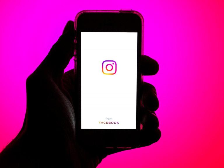 Eine Hand hält ein Smartphone mit dem Instagram Logo auf dem Bildschirm.