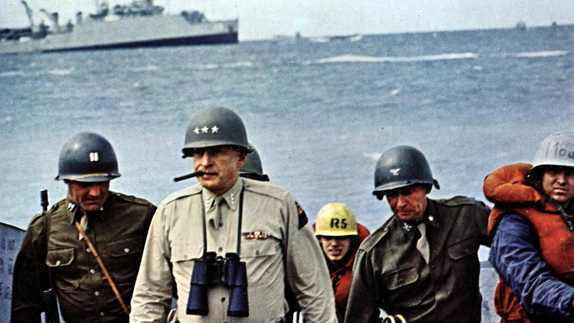 Patton und einige andere Soldaten stehen am Meer, im Hintergrund ist ein Kriegschift zu sehen (Filmstill)