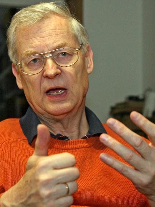 Jürgen Udolph im orangenen Pullover spricht und gestikuliert mit seinen Händen