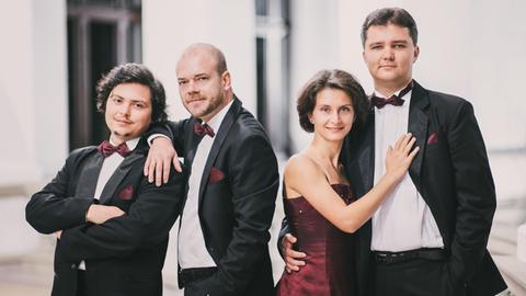 Drei Männer und eine Frau in Konzertkleidung blicken lächelnd in die Kamera.