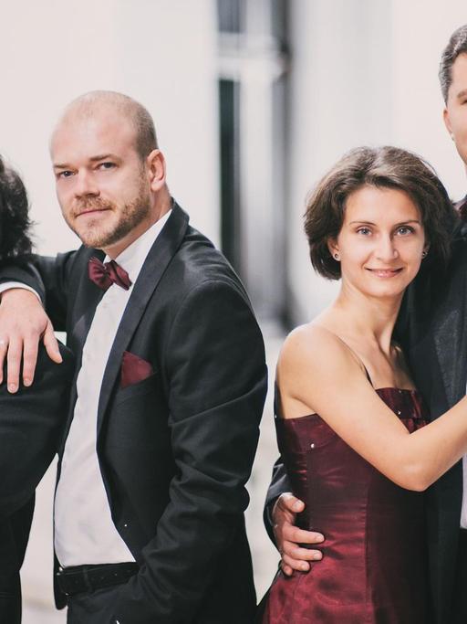 Drei Männer und eine Frau in Konzertkleidung blicken lächelnd in die Kamera.