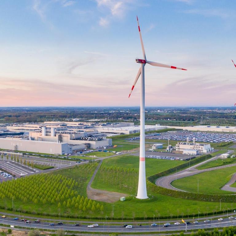 BMW-Mitarbeiter fahren mit ihren Autos zum Werk in Leipzig. Zu sehen sind auf der Luftaufnahme auch Windräder.
