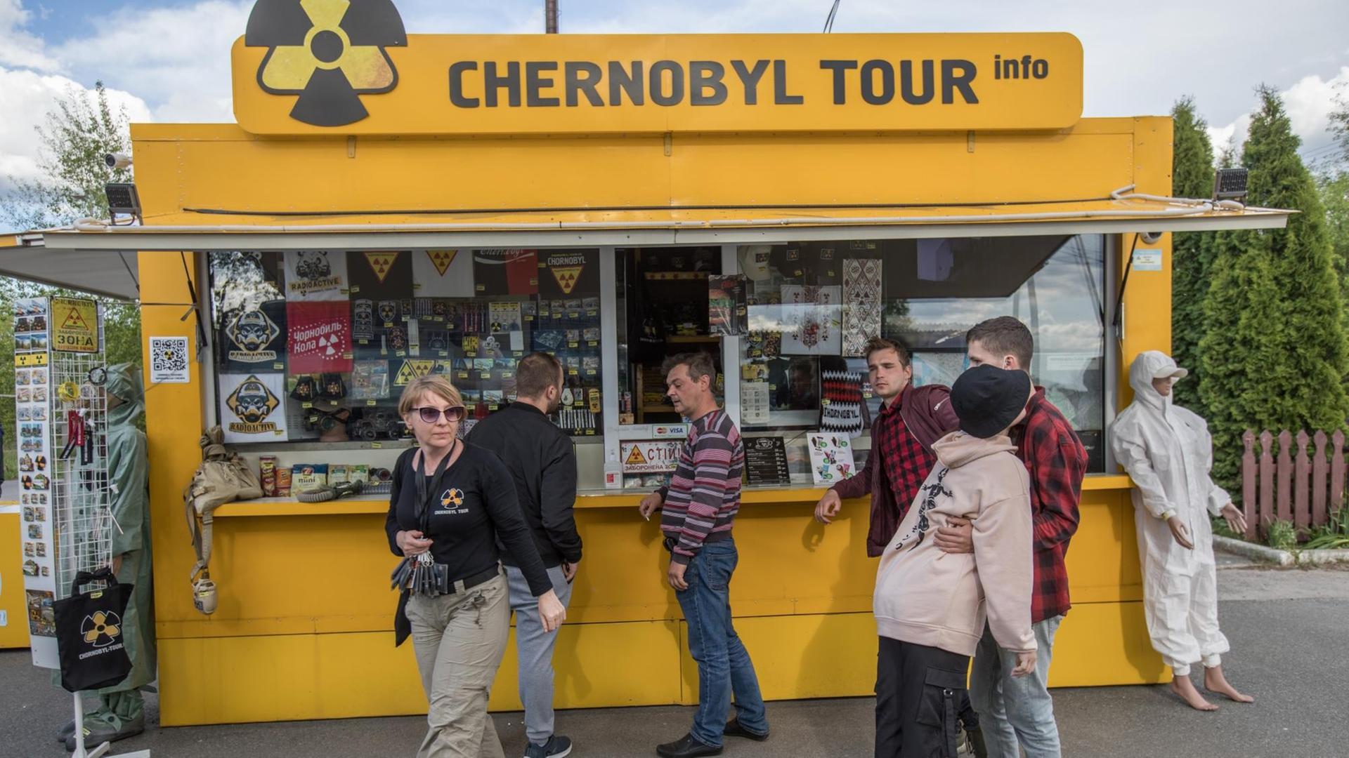 Ein Stand für Touristen im Gebiet des 1986 explodierten Atomkraftwerks Tschernobyl. Er ist gelb mit dem Atomenergie-Symbol. Einige Menschen stehen davor, um sich etwas zu kaufen.