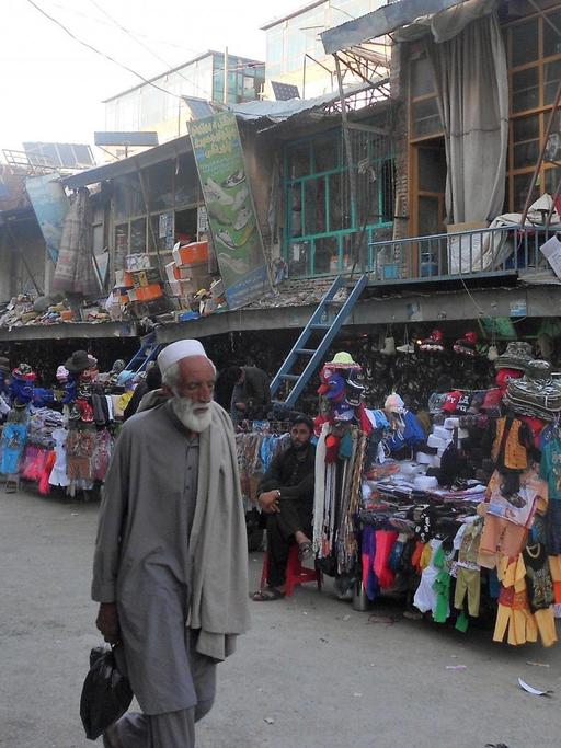 Auf der Einkaufsstraße in Khost stehen Händler mit Kleiderständern, die Häuser sehen kaputt und marode aus.