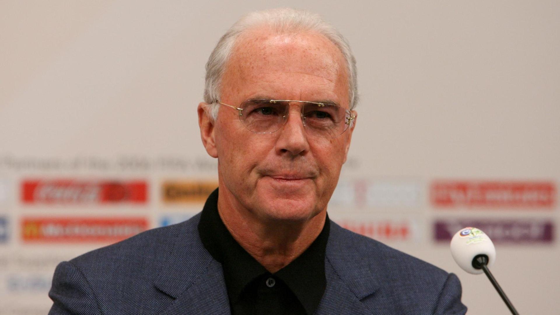 Beckenbauer blickt ernst und spricht in ein Mikrofon.