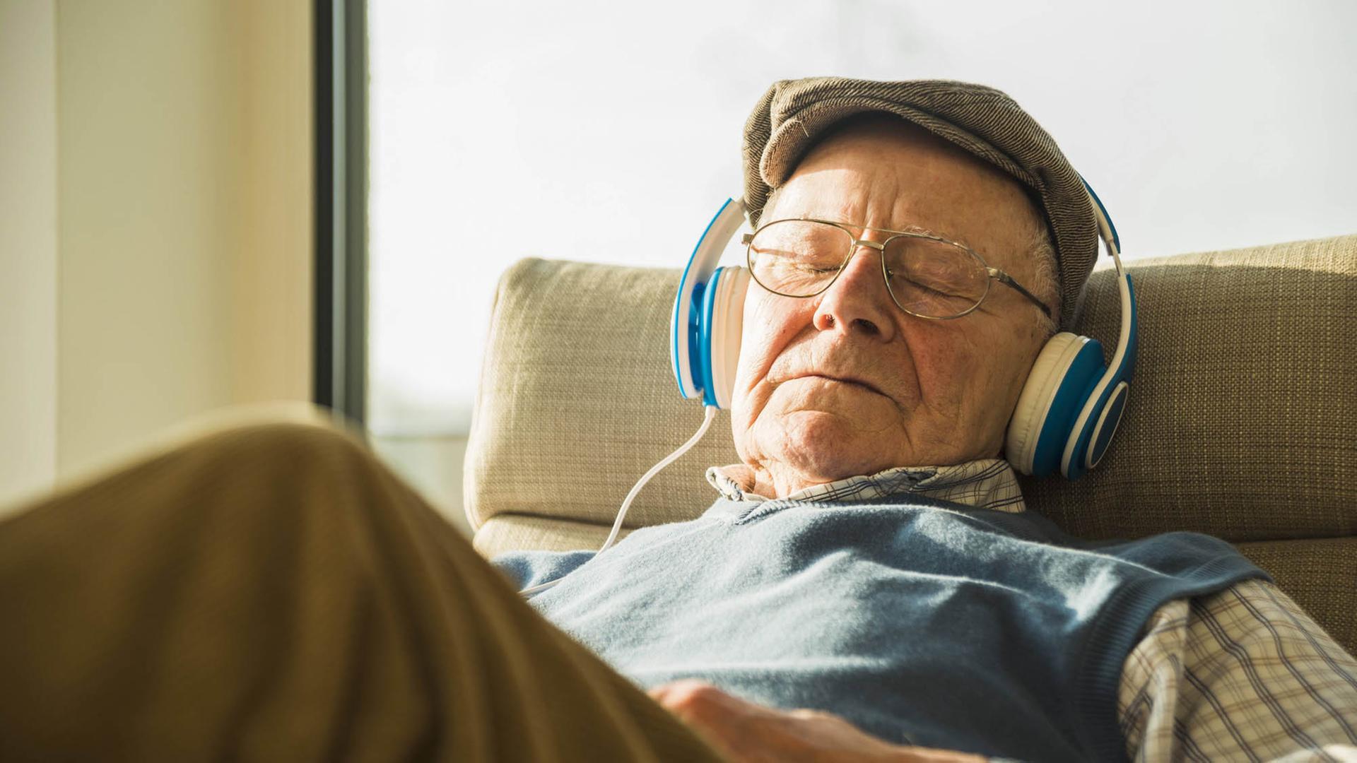 Ein älterer Mann sitzt mit Kopfhörern auf einem Sessel und hört Musik.