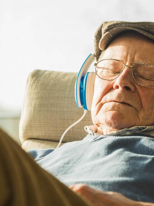 Ein Rentner sitzt mit Kopfhörern auf einem Sessel und hört Musik.