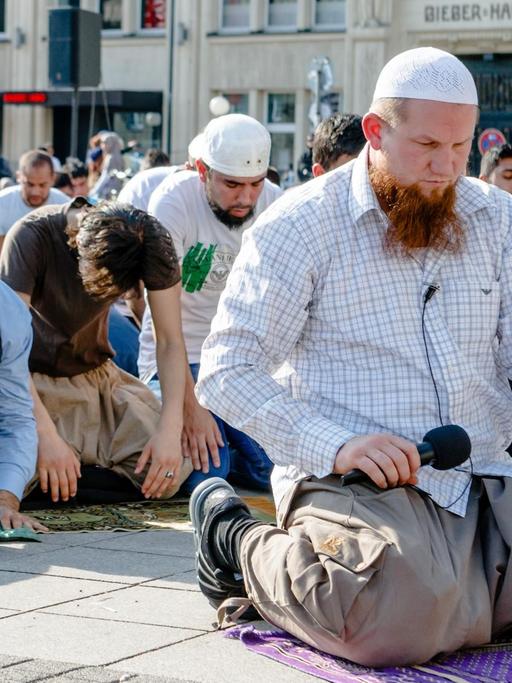 Der salafistische Prediger Pierre Vogel kniet auf dem Boden, hinter ihm beugen sich Dutzende junge Männer betend zu Boden.