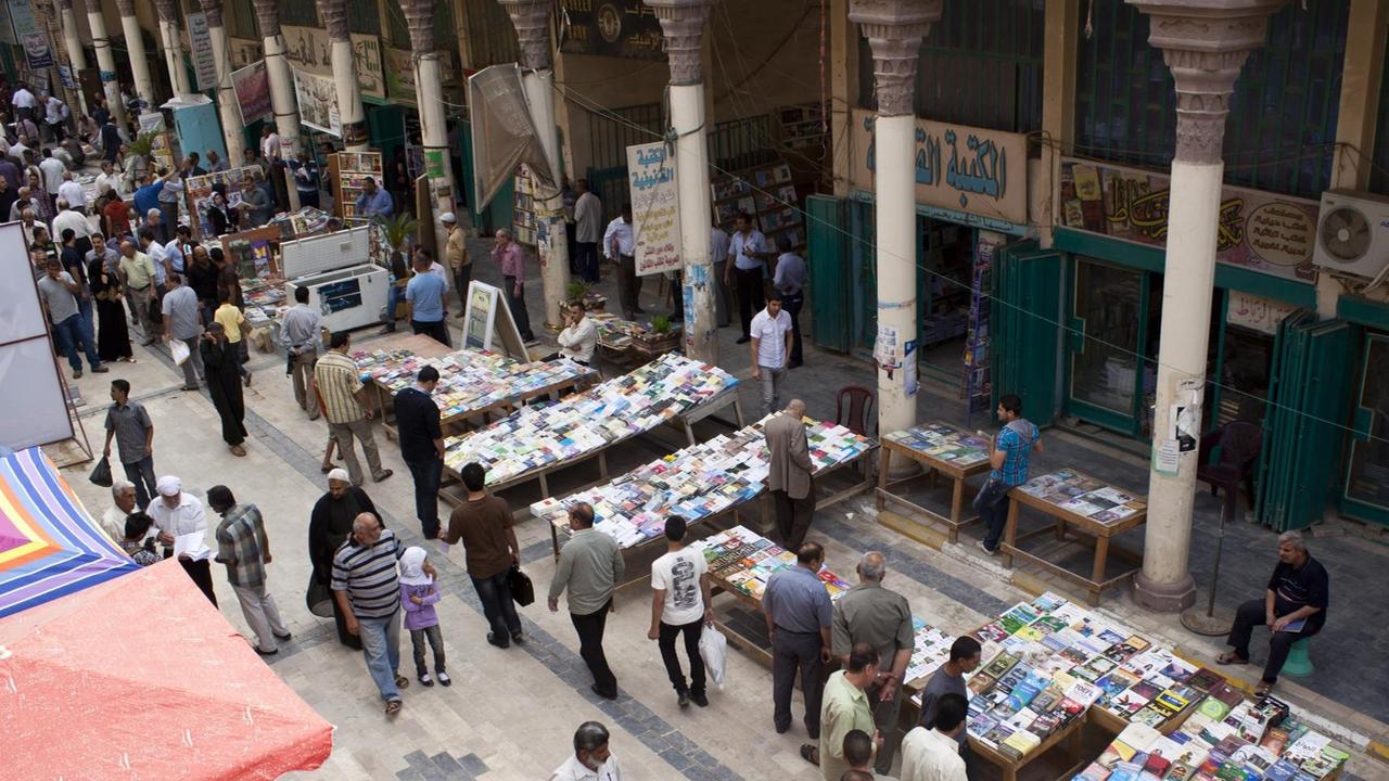 Eine Totale zeigt den Buchmarkt in der Muntanabi-Straße in Bagdad. Zahlreiche Menschen bewegen sich zwischen den Ständen mit Büchern.