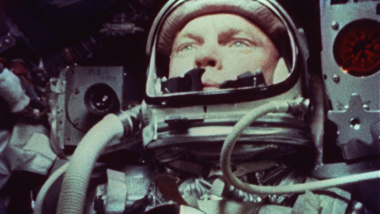 Der Astronaut John Glenn in Anzug, verkabelt und zwischen Technik in einer Raumkapsel sitzend. 