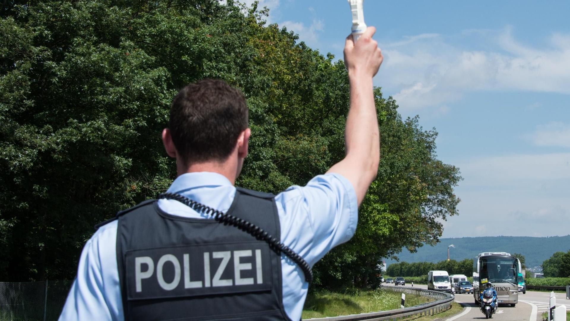 Ein Polizist hält am 09.06.2016 auf einem Autobahnparkplatz während einer Großkontrolle bei Karlsruhe (Baden-Württemberg) einen Bus an. Kurz vor Beginn der Fußball-EM in Frankreich haben rund 130 Polizisten im Großraum Karlsruhe unter anderem nach möglichen Hooligans gefahndet.