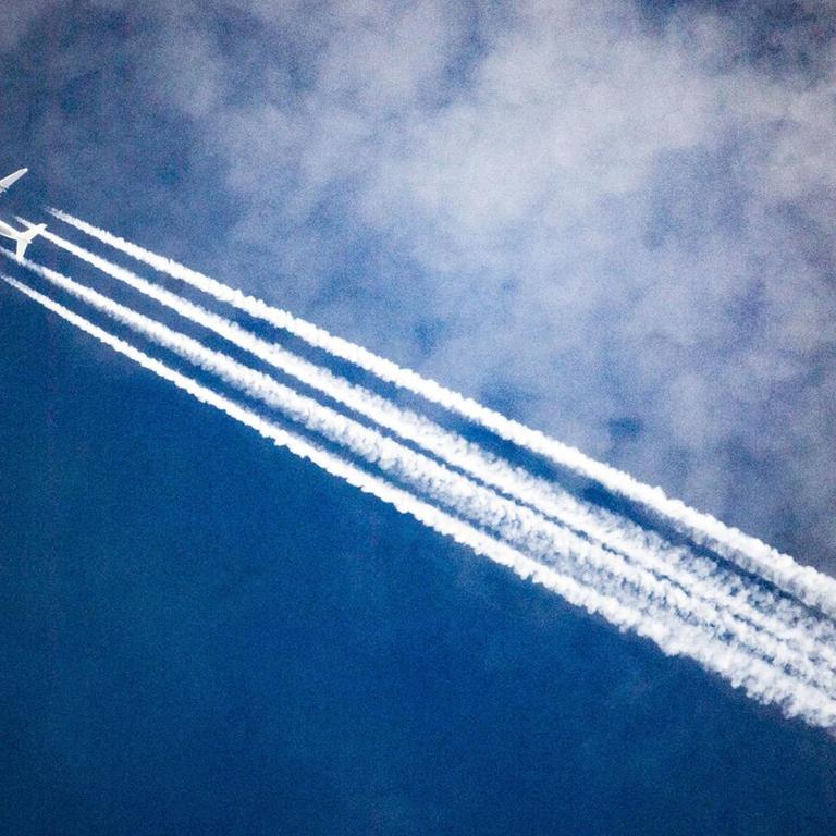 Ein Flugzeug zieht Kondensstreifen hinter sich her, während es durch die Wolken fliegt.