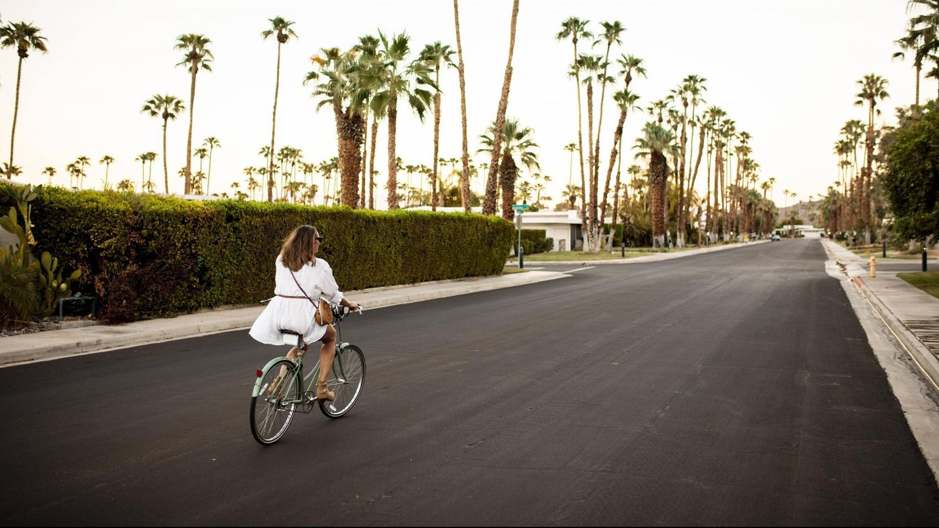 Eine Frau fährt auf einer von Palmen gesäumten Straße in Palm Springs Rad.