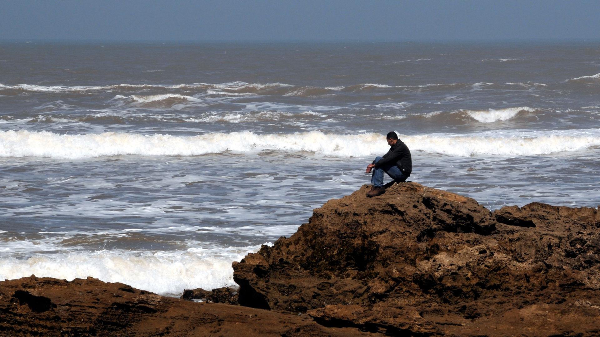 Ein Mann sitzt auf einem Felsen an einer Meeresküste 