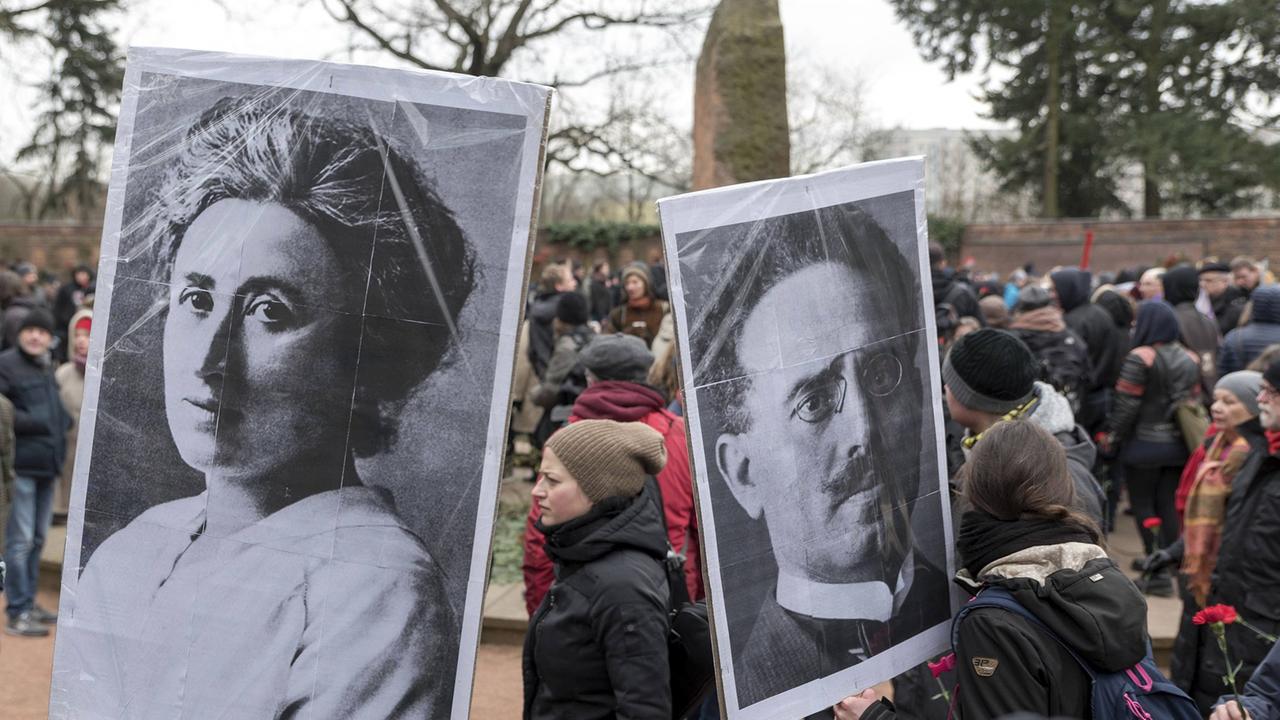 Demonstranten stehen 2018 mit Bildern von Rosa Luxemburg und Karl Liebknecht anlässlich des 99. Jahrestages ihrer Ermordung vor der Gedenkstätte der Sozialisten in Berlin-Friedrichsfelde.