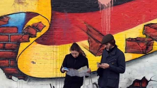 Passanten stehen in Berlin an einem Wandbild mit der deutschen Nationalflagge.
