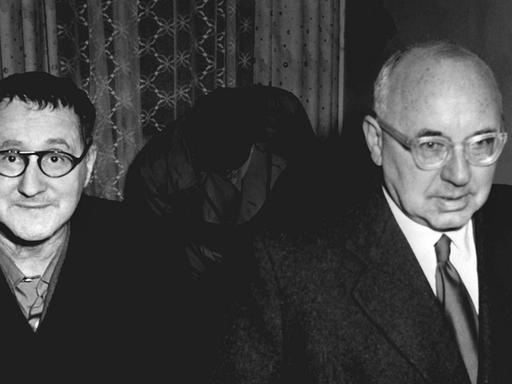 Eine schwarz-weiß-Fotografie zeigt Bertolt Brecht und Johannes R. Becher, wie sie 1954 gemeinsam durch ein Hotelzimmer laufen.