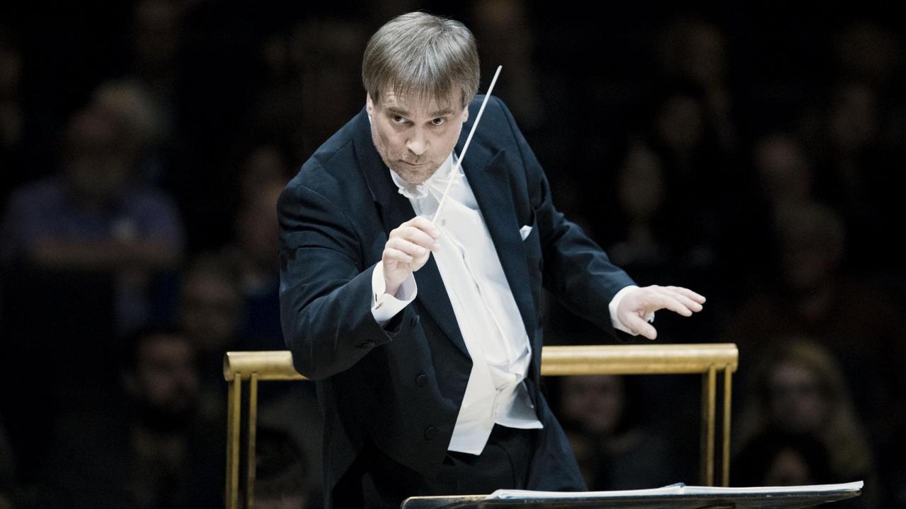 Der Dirigent John Storgårds dirigiert im Frack mit Taktstock auf dem Konzertpodium