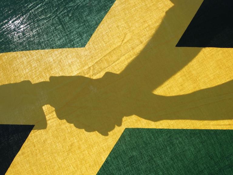 Drei Hände vereinigen sich am in Frankfurt hinter der Landesfahne von Jamaika in den Farben schwarz, gelb und grün.